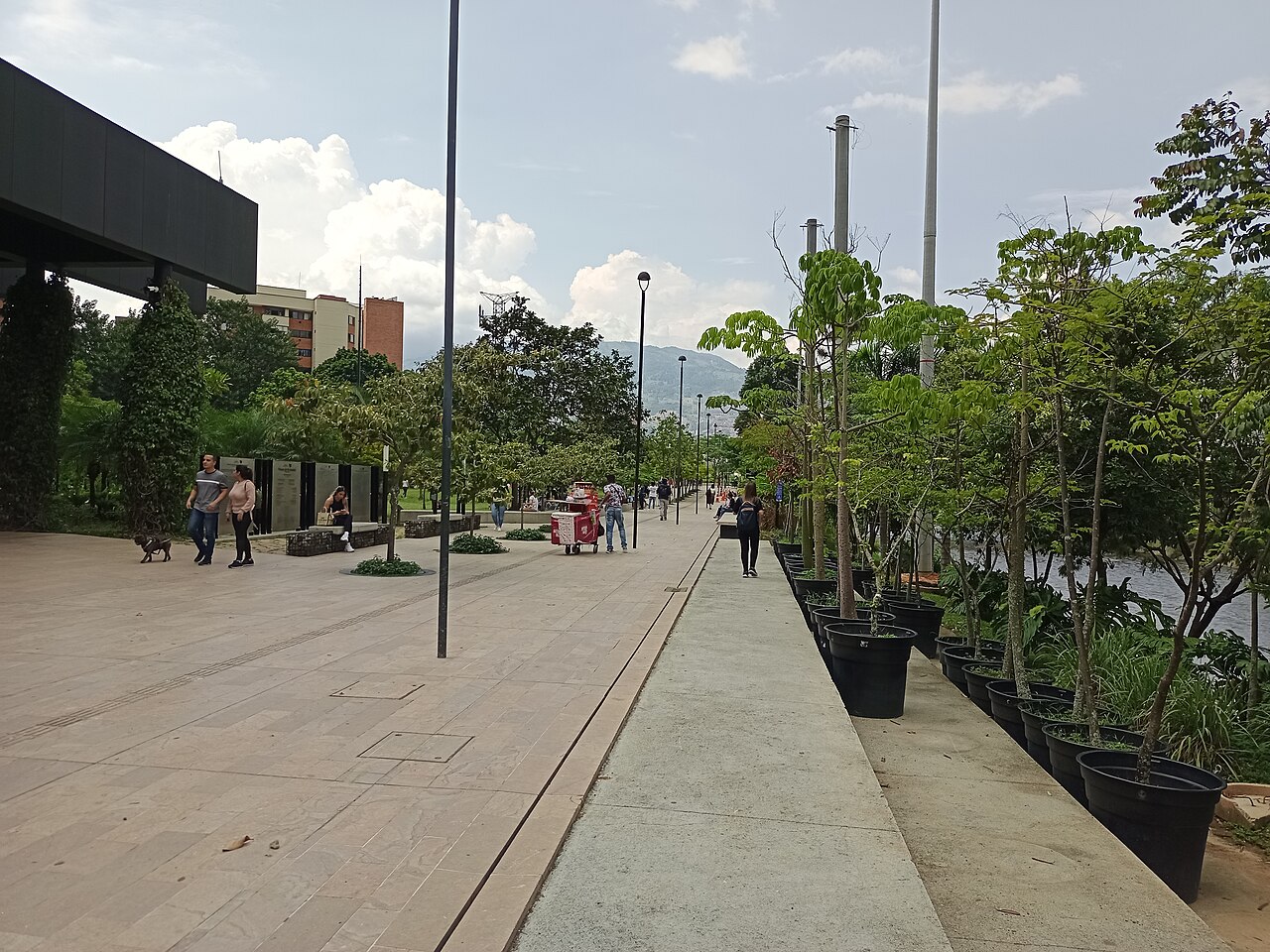 Pedestrian promenade at Parques del Río Medellín in October 2023, lined with trees and planters along the river